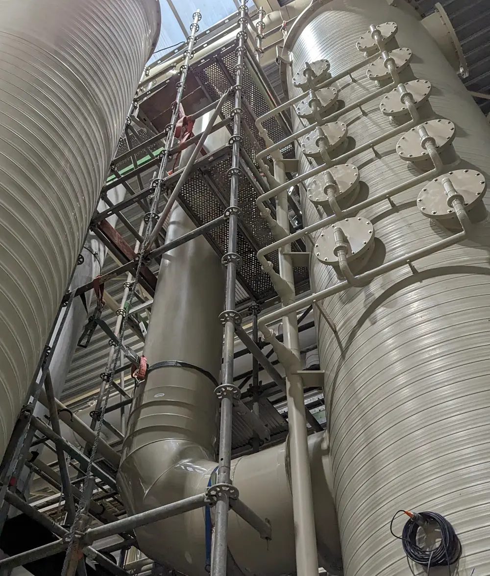 Interior view of the odour-control installation: large white scrubber columns and ventilation ducting with a row of flanged nozzle connections and steel access scaffolding.